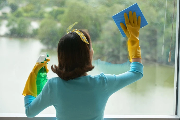 Person cleaning window glass with cloth and spray